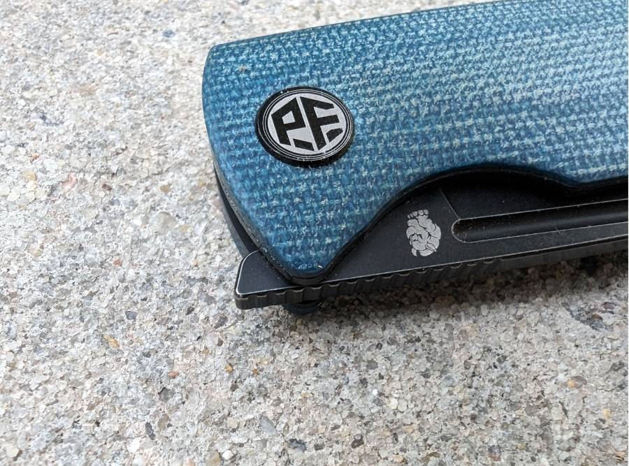 Close-up of Petrified Fish Beluga PFP01 knife with blue micarta handle and PF logo on pivot.