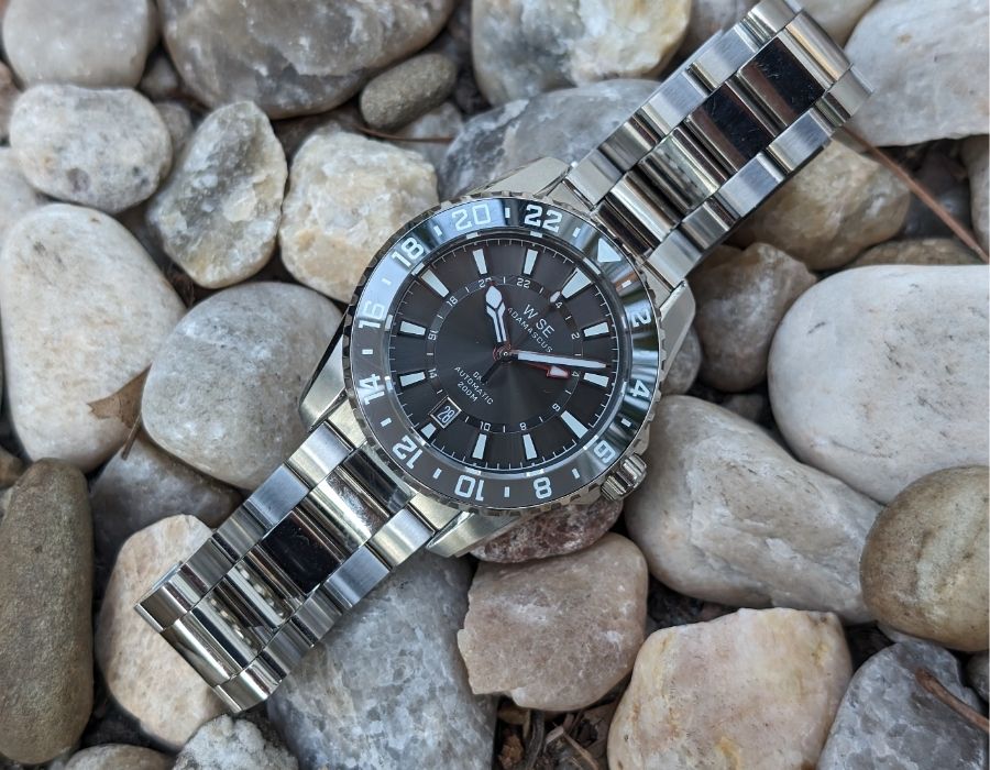 WISE ADX 110 True GMT automatic wristwatch with stainless steel bracelet displayed on rocks